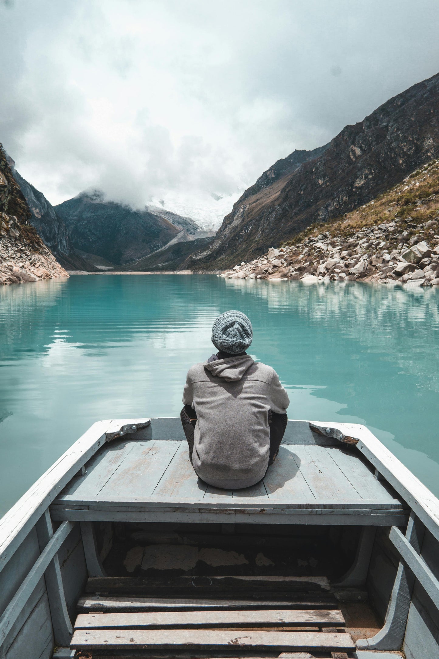 Person sitting on a boat overlooking a serene lake with mountains in the background