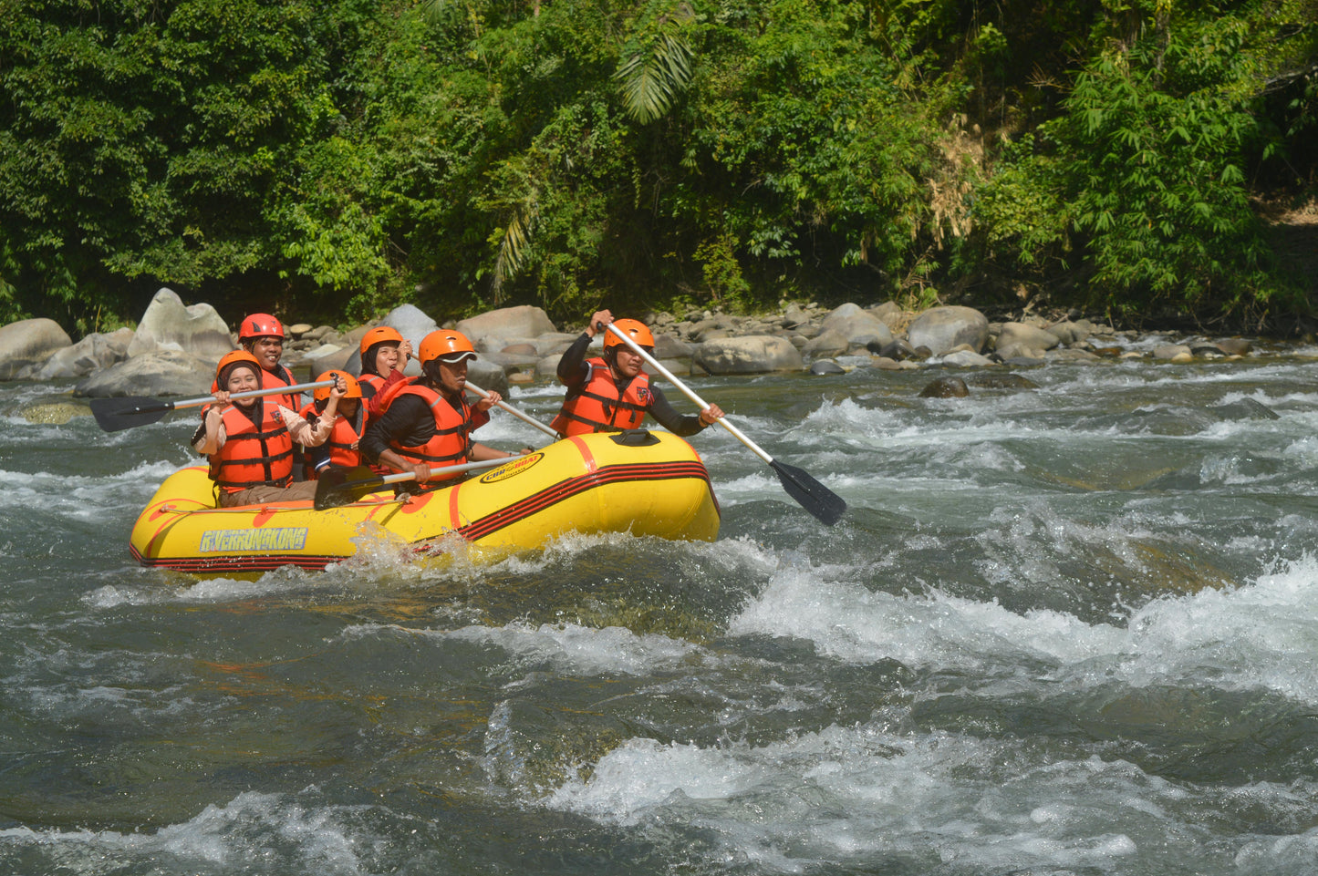 Group of people rafting in a yellow boat on a river with rocky banks and greenery.