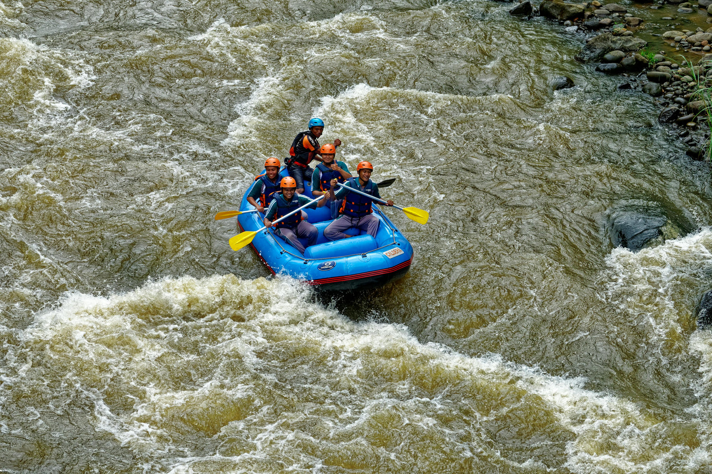 Group of people rafting in a blue inflatable raft on turbulent river water.