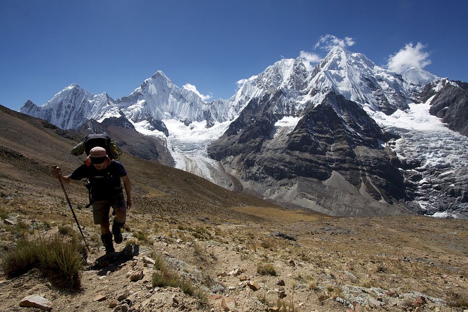 Hiker with backpack and walking stick on a mountain trail with snow-capped peaks in the background