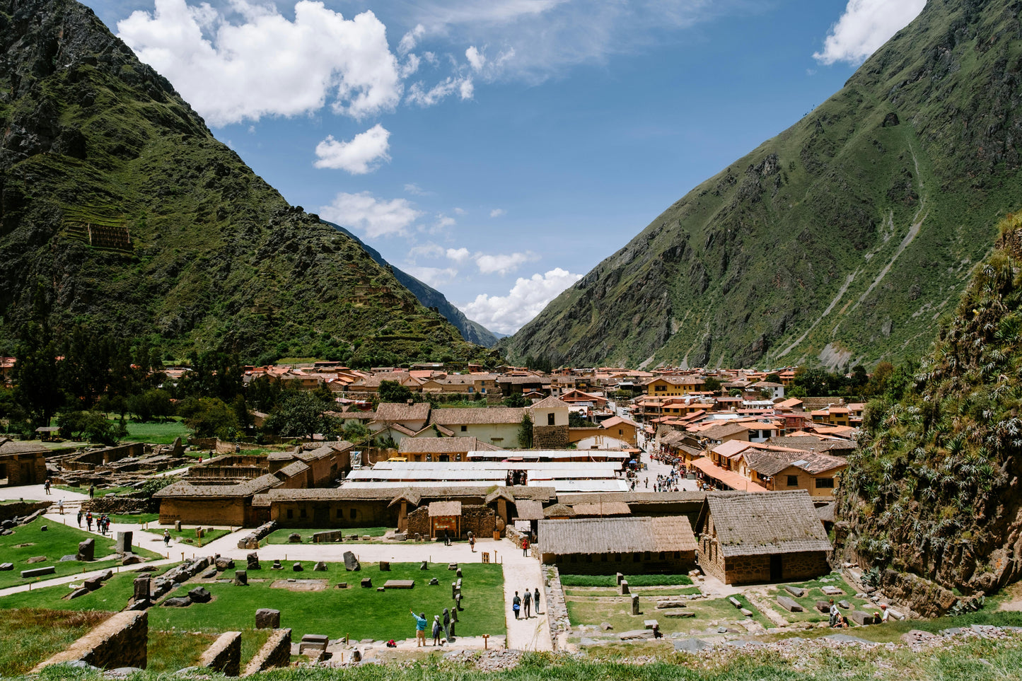 Ancient Incan ruins in a mountainous valley with greenery and clear blue sky.