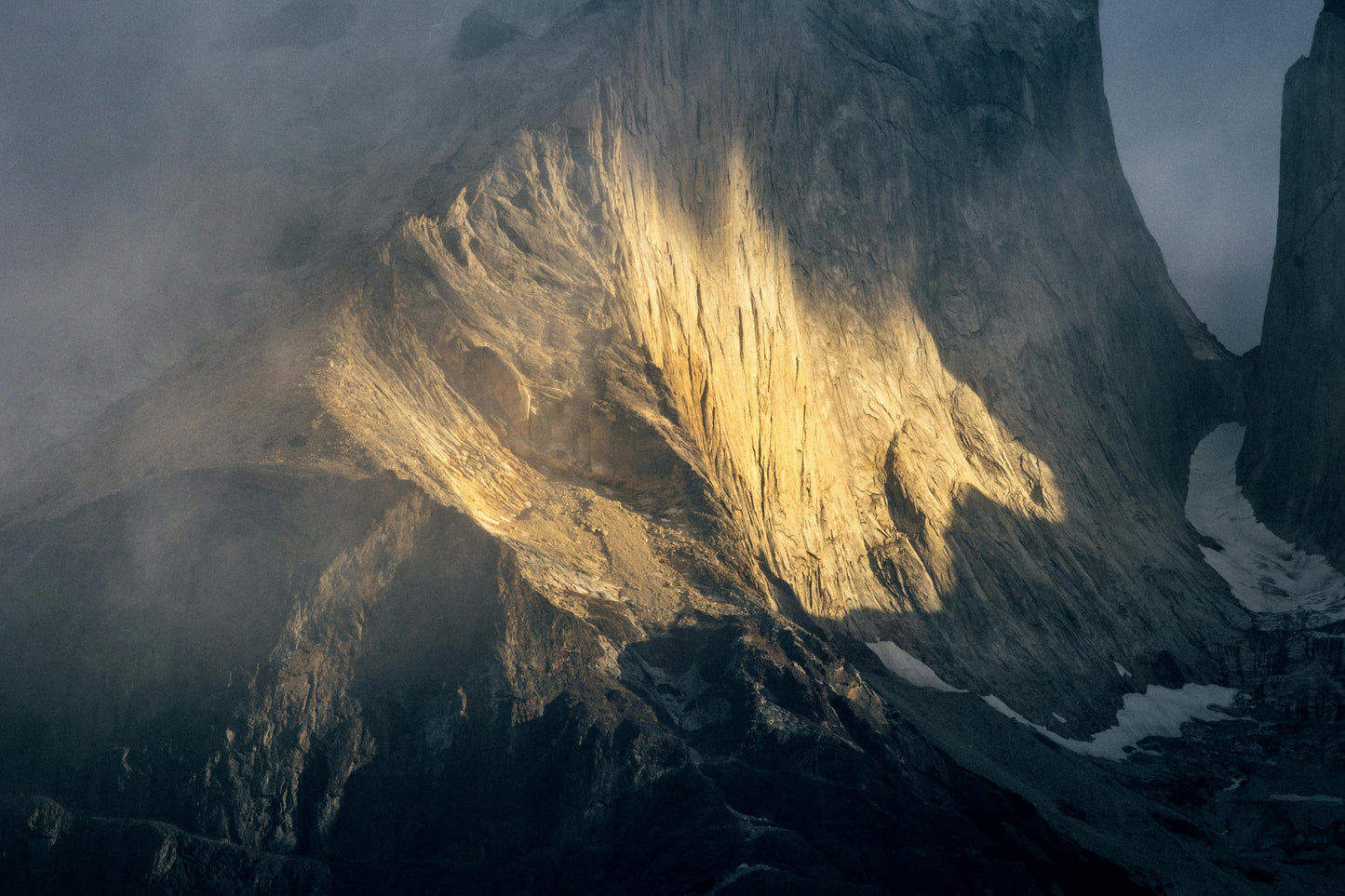 Sunlight illuminates a rugged mountain peak with snow patches.