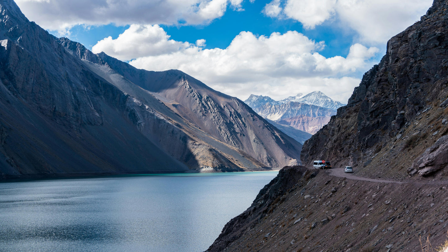 Mountainous landscape with a lake and road, featuring vehicles.
