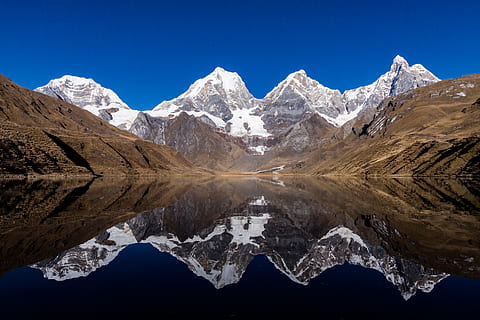 Snow-capped mountains reflected in a calm lake with clear blue sky