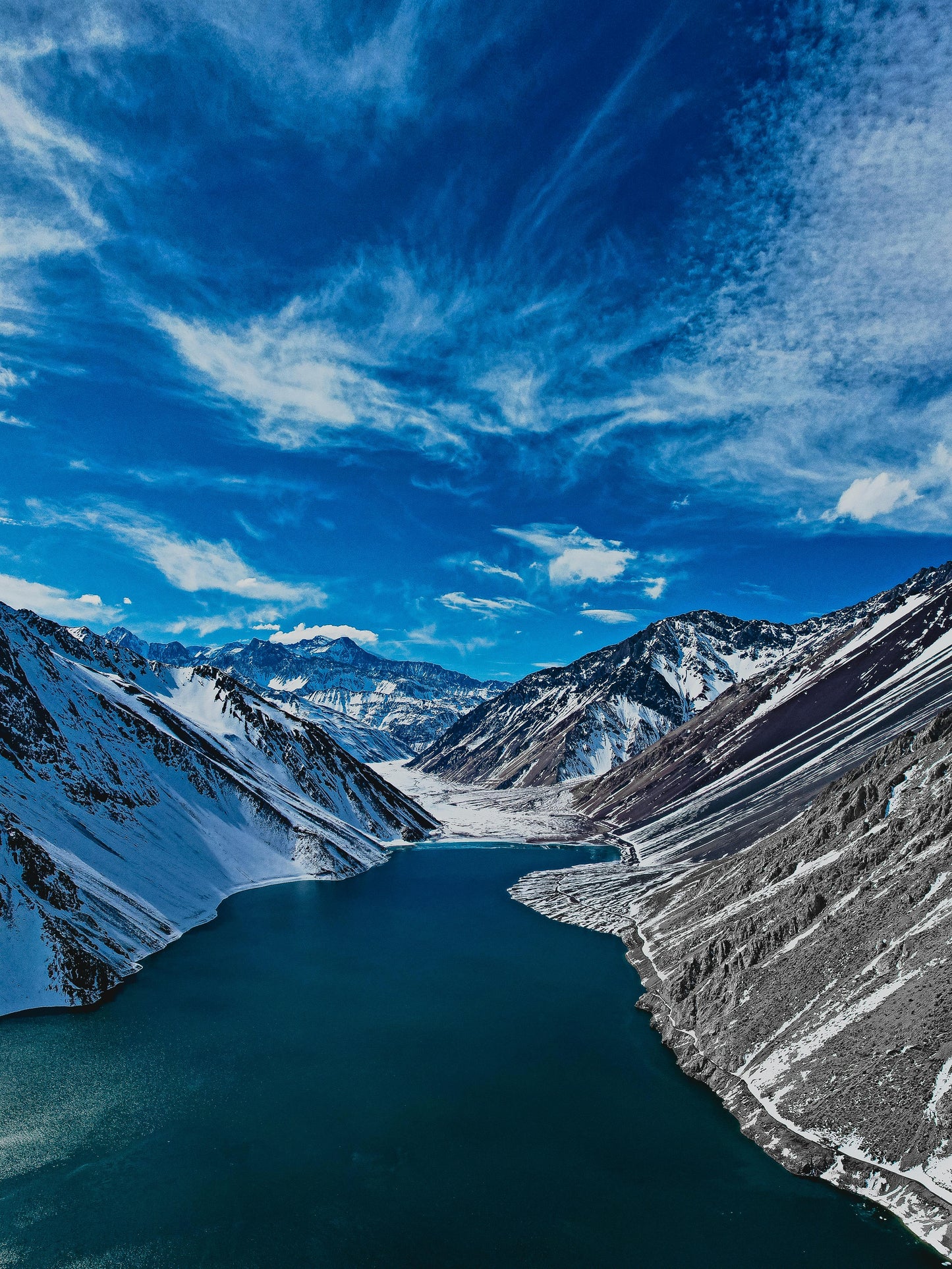 Mountain landscape with a lake and snow-capped peaks under a blue sky.