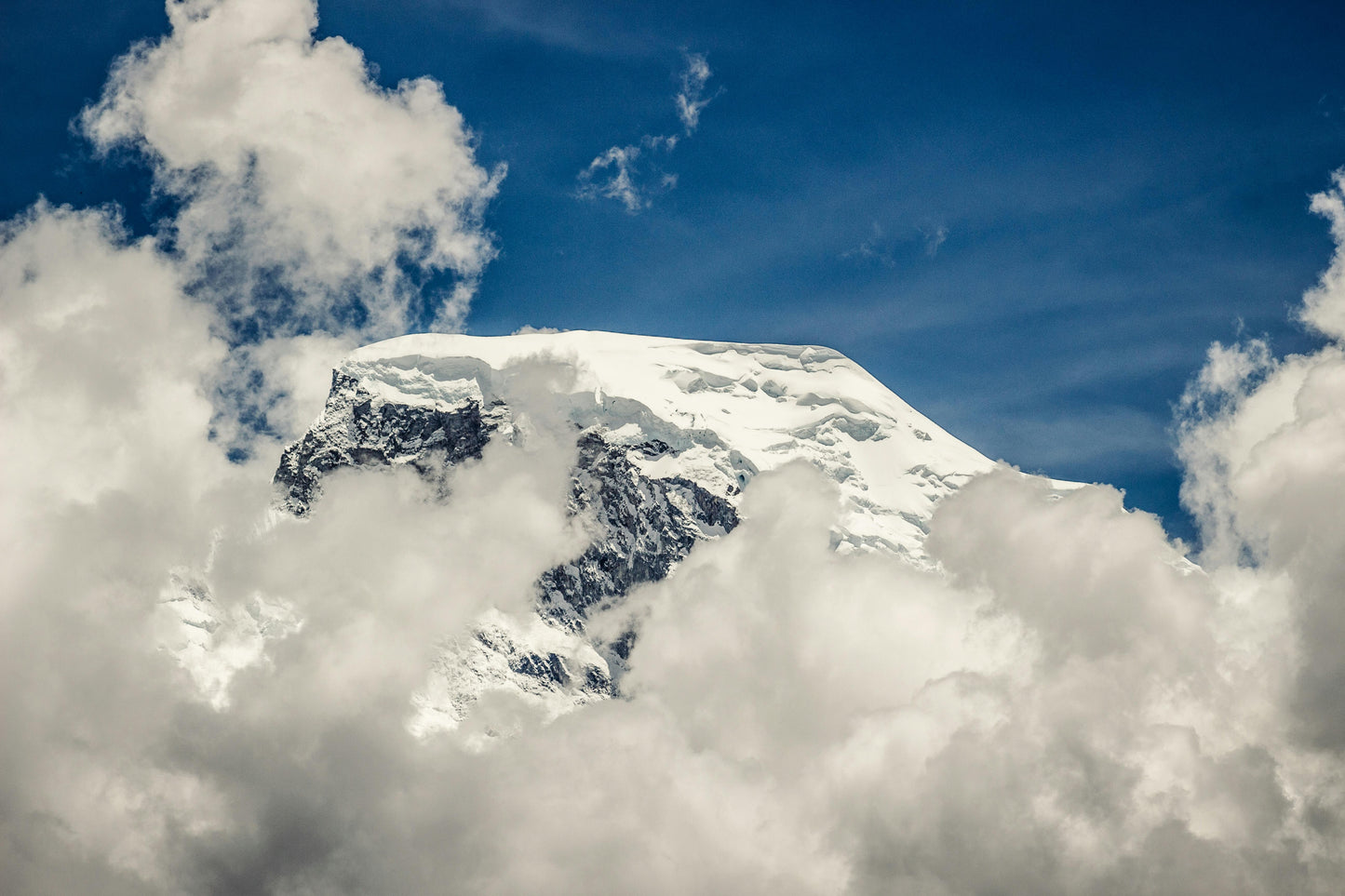 Snow-capped mountain peak surrounded by clouds with a blue sky.