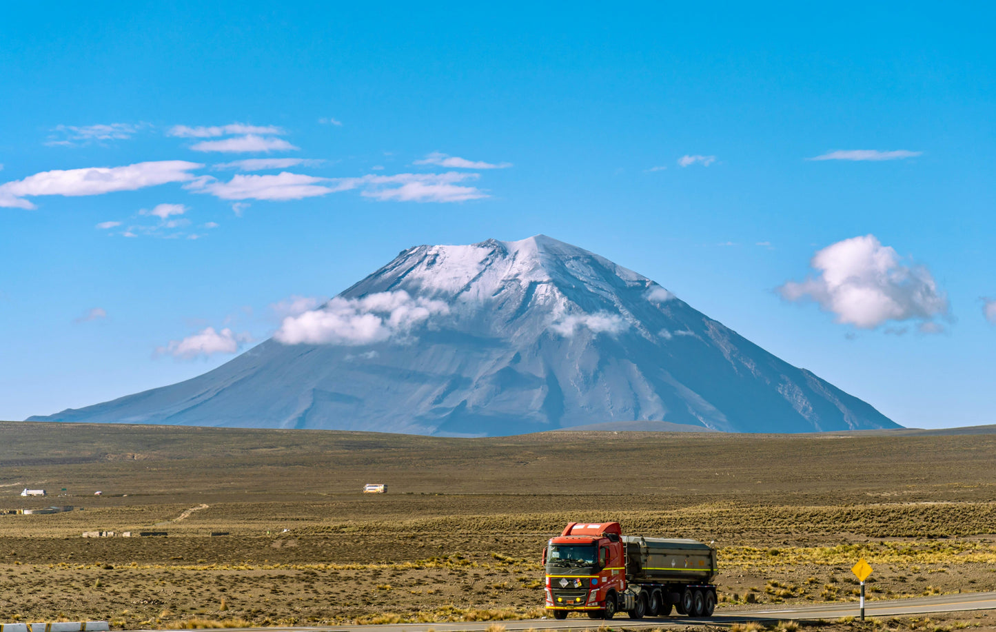 Truck on a road with a mountain in the background under a clear blue sky.