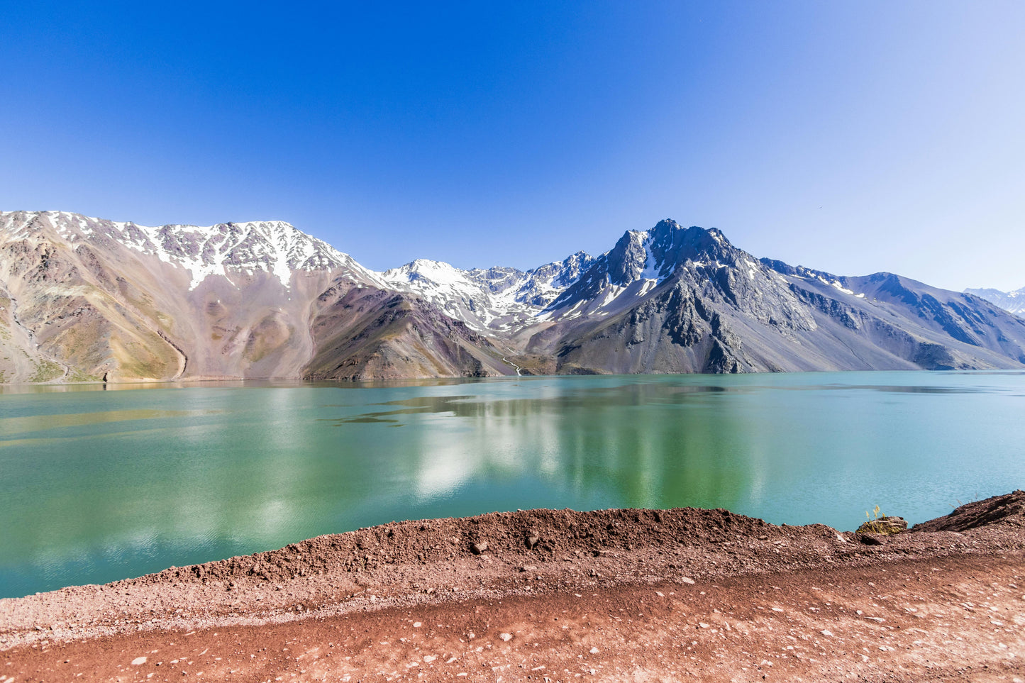 Mountain lake with clear blue water and snow-capped peaks under a bright blue sky.