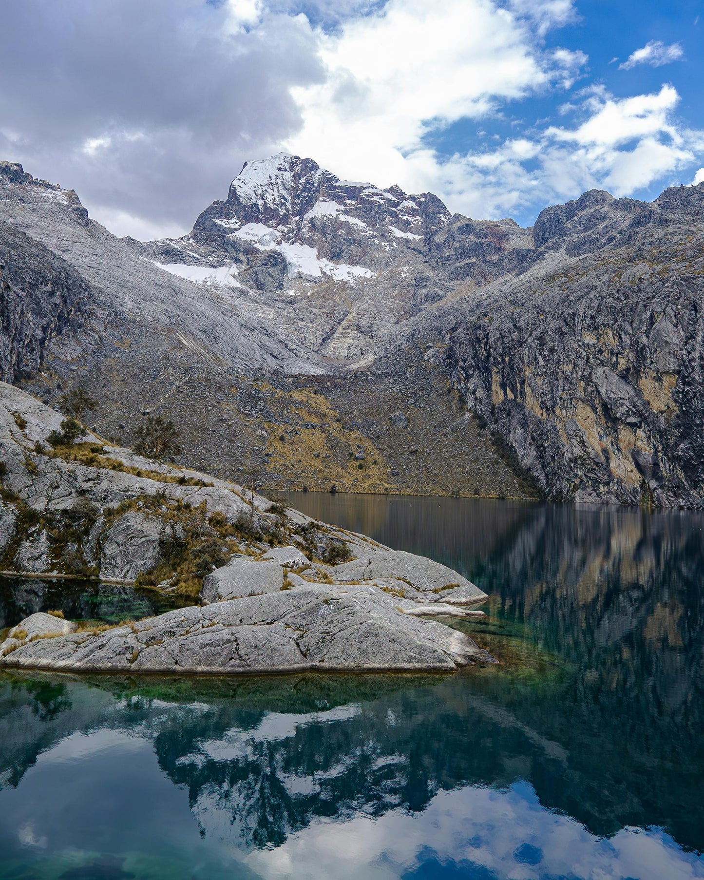 Mountainous landscape with a lake and snow-capped peaks under a blue sky.