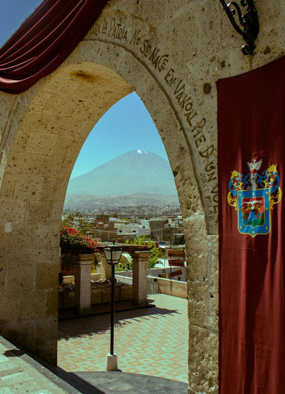 View through a stone archway with a mountain in the background, featuring a coat of arms on a red curtain.