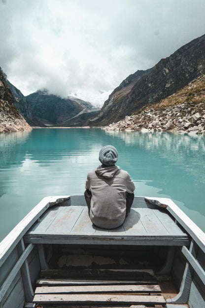 Person sitting on a boat overlooking a serene lake with mountains in the background