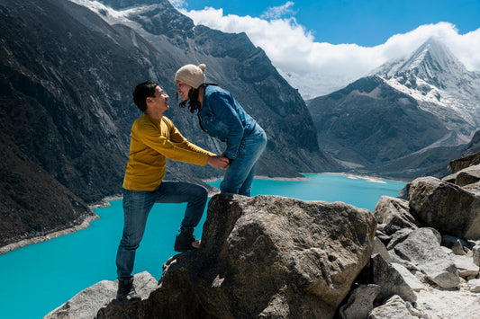 Two people on a rocky outcrop with a scenic mountain and lake background