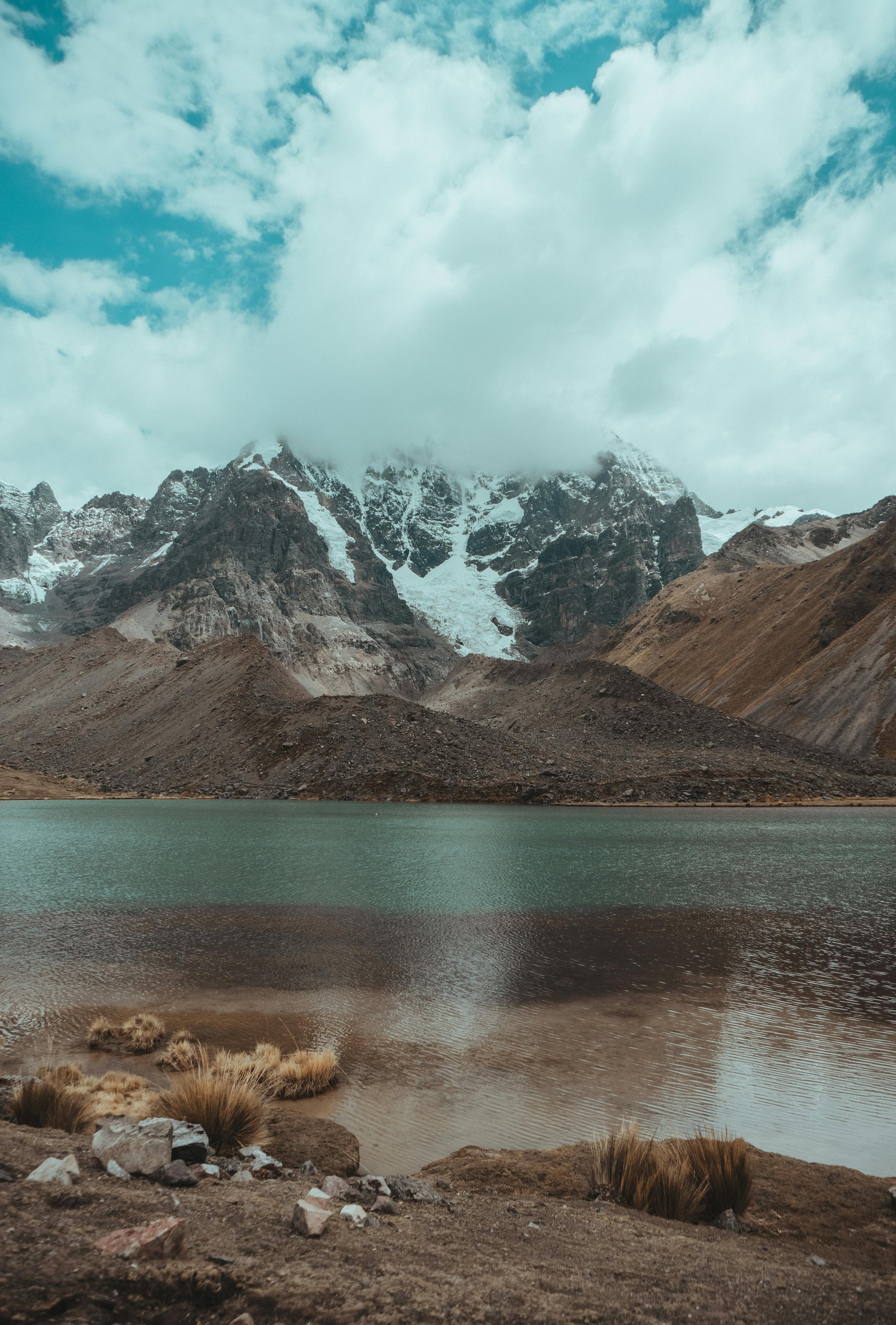Mountain landscape with a lake and snow-capped peaks under a cloudy sky