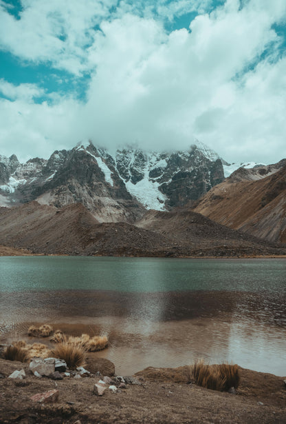 Mountain landscape with a lake and snow-capped peaks under a cloudy sky