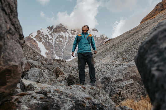 Person hiking on a rocky mountain trail with snow-capped peaks in the background