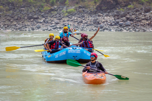 Group of people rafting on a river with a blue raft and an orange kayak.