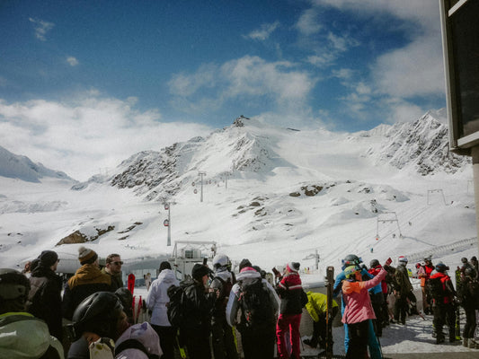 Group of people gathered in a snowy mountainous area with ski lifts and snow-covered peaks.