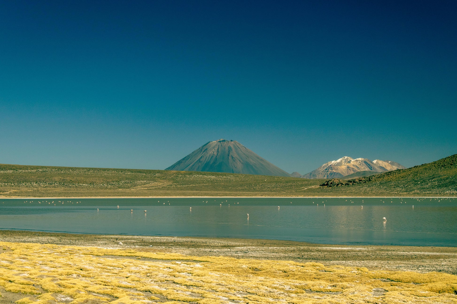 Landscape with a lake, grassy area, and mountains under a clear blue sky.