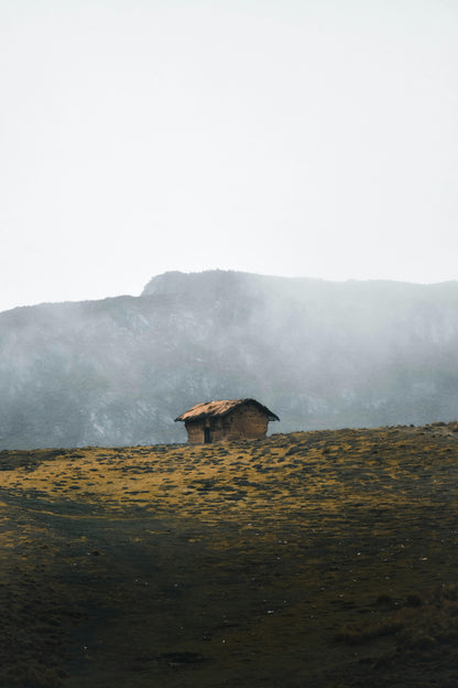 Small cabin on a grassy hill with mountains in the background
