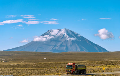 Truck on a road with a mountain in the background under a clear blue sky.