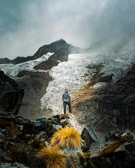 Person standing on a rocky outcrop with a mountainous landscape and glacier in the background