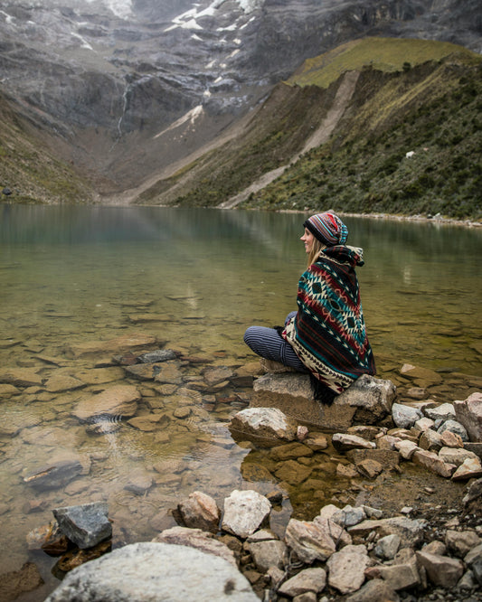 Person sitting by a lake with mountains in the background