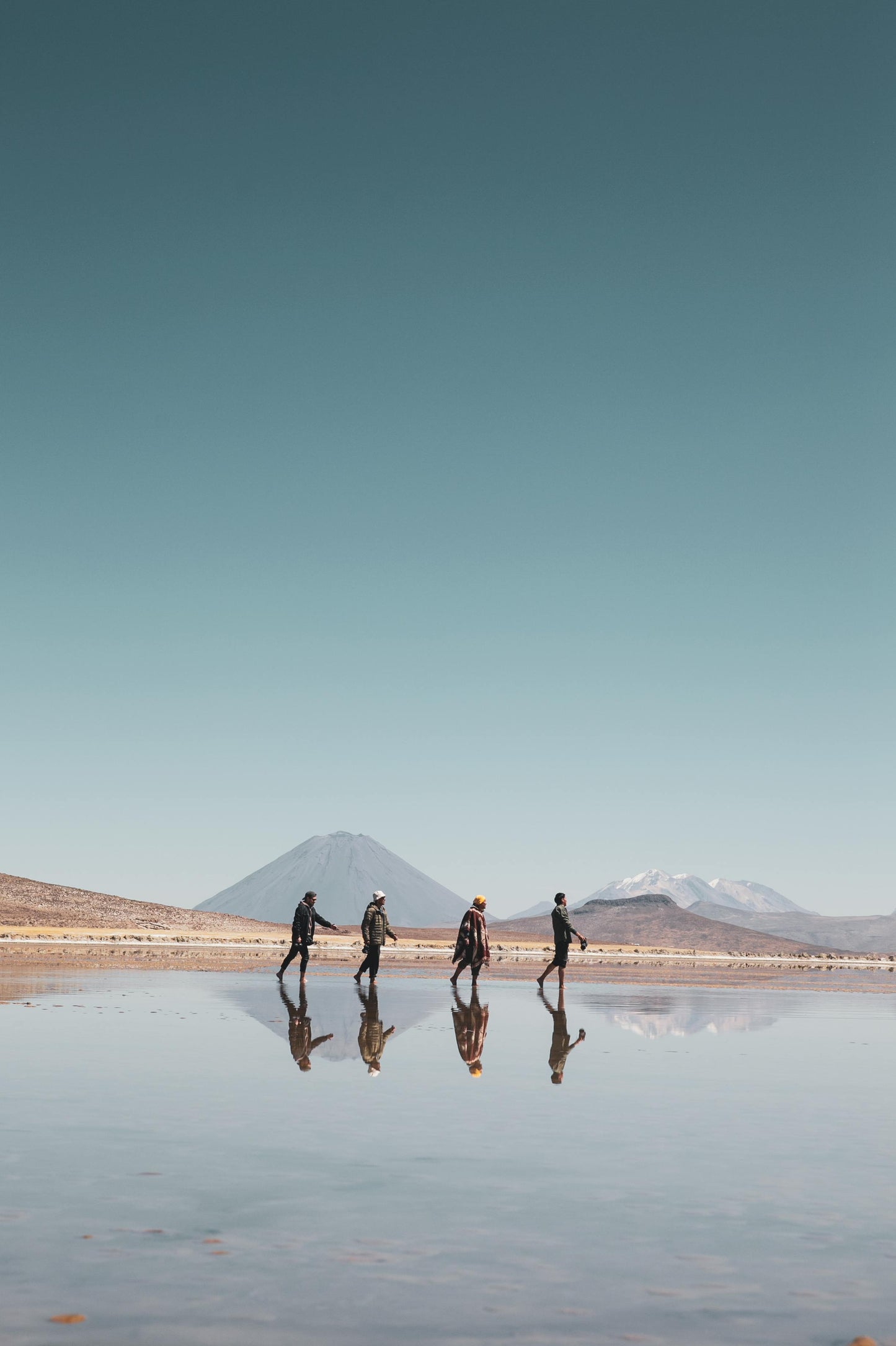 Four people walking on a reflective water surface with mountains in the background