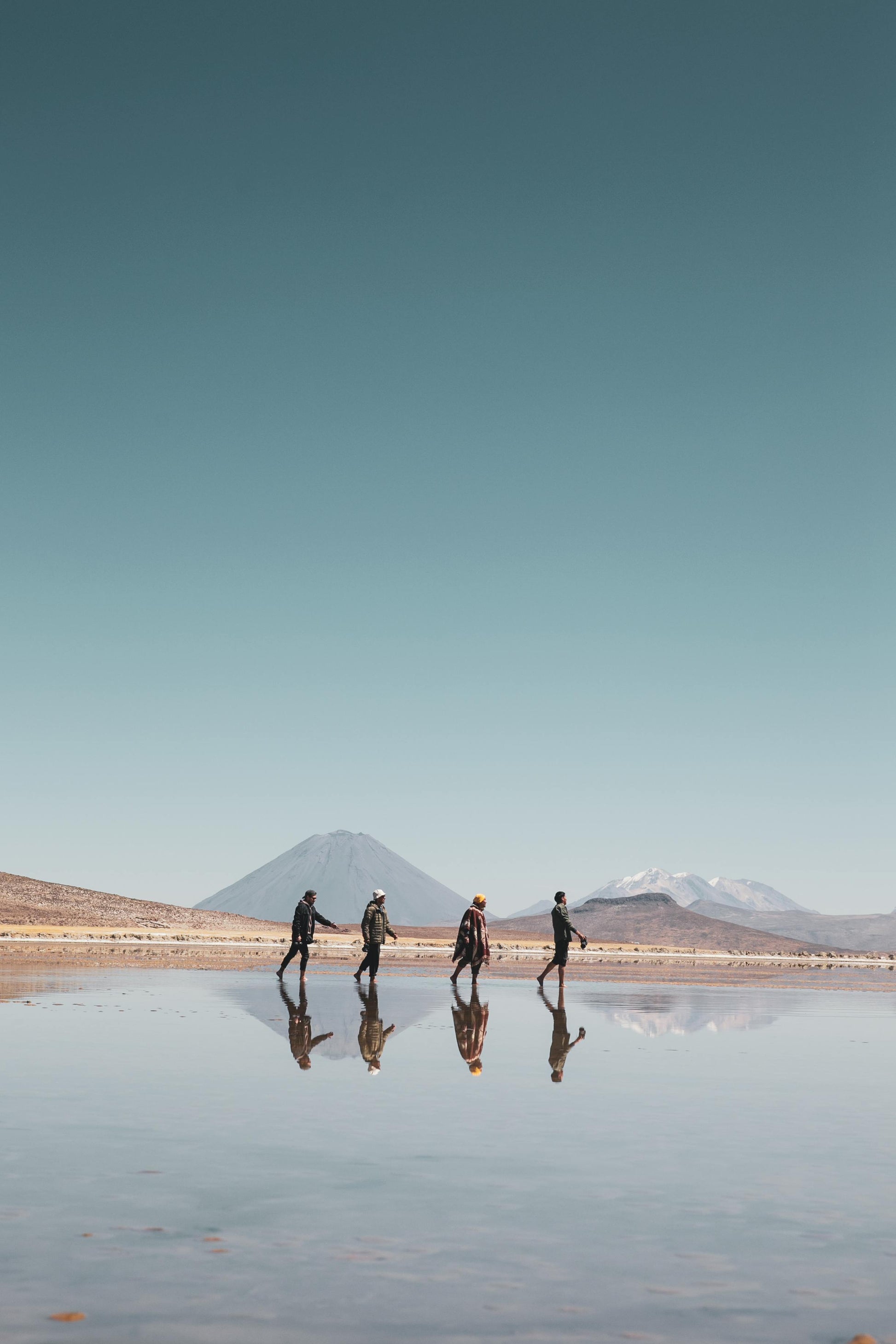 Four people walking on a reflective water surface with mountains in the background