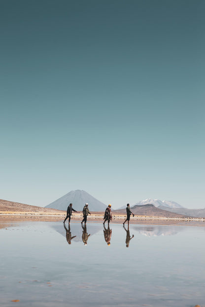 Four people walking on a reflective water surface with mountains in the background