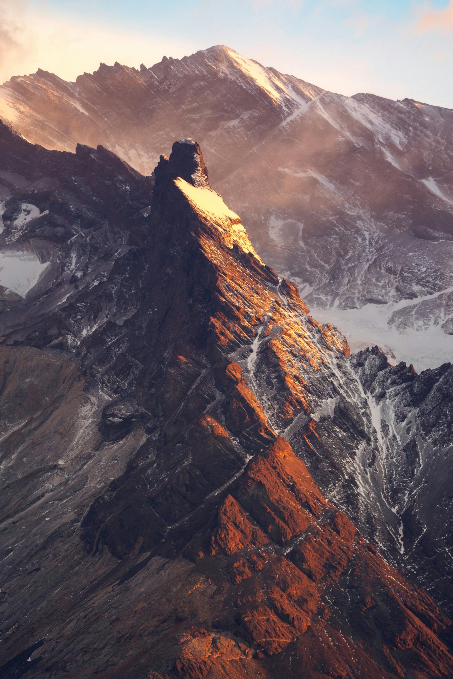 Mountain peak with a rugged surface and snow patches at sunset.